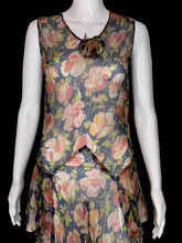 Load image into Gallery viewer, A sleeveless dress with a floral print. The dress features a navy blue base with pink, red, and green floral patterns, and a ruffled asymmetrical hem.
