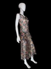 Load image into Gallery viewer, A sleeveless dress with a floral print. The dress features a navy blue base with pink, red, and green floral patterns, and a ruffled asymmetrical hem.
