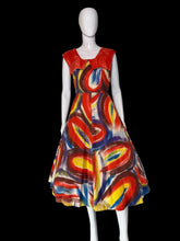 Load image into Gallery viewer, A sleeveless A-line dress displayed on a white mannequin. The dress features a bold abstract swirl pattern in red, blue, yellow, and white, with a solid red V-neckline on the back and dramatic collar. 
