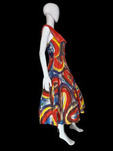 Load image into Gallery viewer, A sleeveless A-line dress displayed on a white mannequin. The dress features a bold abstract swirl pattern in red, blue, yellow, and white, with a solid red V-neckline on the back and dramatic collar. 
