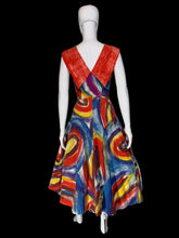 Load image into Gallery viewer, A back view of a sleeveless A-line dress displayed on a white mannequin. The dress features a bold abstract swirl pattern in red, blue, yellow, and white, with a solid red V-neckline on the back and dramatic collar. 
