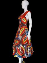 Load image into Gallery viewer, A sleeveless A-line dress displayed on a white mannequin. The dress features a bold abstract swirl pattern in red, blue, yellow, and white, with a solid red V-neckline on the back and dramatic collar. 
