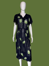 Load image into Gallery viewer, A short-sleeve midi dress displayed on a white mannequin. The dress is navy blue with a green leaf print and small cream, teal, and blue speckled details.
