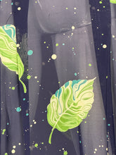 Load image into Gallery viewer, A close-up of a dark navy dress featuring a pattern of green and light green leaves with teal, cream,and green paint splatter details.
