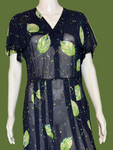 Load image into Gallery viewer, A sheer navy blue V-neck dress displayed on a white mannequin, featuring a green leaf print and small scattered cream, green, and teal speckles.
