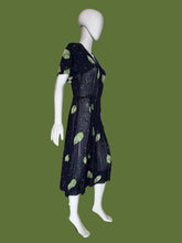Load image into Gallery viewer, A sheer navy blue V-neck dress displayed on a white mannequin, featuring a green leaf print and small scattered cream, green, and teal speckles.
