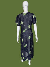 Load image into Gallery viewer, A sheer navy blue V-neck dress displayed on a white mannequin, featuring a green leaf print and small scattered cream, green, and teal speckles.
