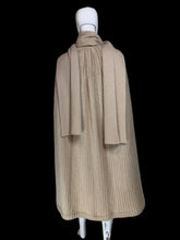 Load image into Gallery viewer, A beige ribbed knit cape with a draped collar and layered hem, displayed on a white mannequin.
