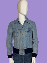 Load image into Gallery viewer, A light blue denim jacket with dark navy ribbed trim at the collar, cuffs, and hem, displayed on a white mannequin. 
