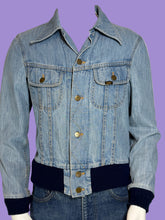 Load image into Gallery viewer, A close up of a light blue denim jacket with dark navy ribbed trim at the collar, cuffs, and hem, displayed on a white mannequin.
