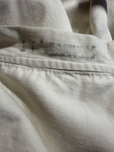 Load image into Gallery viewer, Close-up of an off-white or cream-colored fabric garment, showing a stitched seam and faint stamped markings in dark ink.

