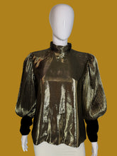 Load image into Gallery viewer, A metallic gold pleated blouse with black long sleeves and a high mock neck, shown on a white mannequin.
