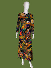 Load image into Gallery viewer, A long-sleeve maxi dress with a vibrant, dense floral and paisley print on a black base, displayed on a white mannequin.

