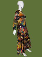Load image into Gallery viewer, A long-sleeve maxi dress with a vibrant, dense floral and paisley print on a black base, displayed on a white mannequin.

