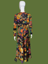 Load image into Gallery viewer, A long-sleeve maxi dress with a vibrant, dense floral and paisley print on a black base, displayed on a white mannequin.
