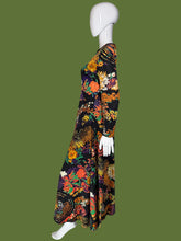 Load image into Gallery viewer, A long-sleeve maxi dress with a vibrant, dense floral and paisley print on a black base, displayed on a white mannequin.
