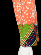 Load image into Gallery viewer, A close-up of a small stain on the sleeve of a patchwork dress featuring multiple colorful patterns, including a green floral print, an orange floral print, and striped plaid panels.
