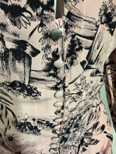 Load image into Gallery viewer, Close-up of a garment featuring a black and pink  floral print, a vertical zipper, and a decorative row of buttons down the center.
