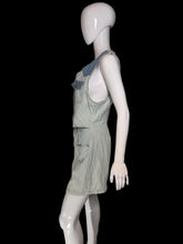 Load image into Gallery viewer, A light gray denim overall romper displayed on a white mannequin, shown from a side profile against an indoor wall.
