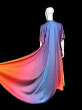 Load image into Gallery viewer, A long flowing dress displayed on a mannequin. The garment has a vertical gradient transitioning from purple and blue at the top, through pink, to bright orange and yellow at the bottom.
