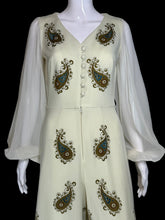 Load image into Gallery viewer, An off-white sleeveless jumpsuit with sheer long sleeves, featuring brown and teal paisley embroidery and a button-up front, displayed on a white mannequin.
