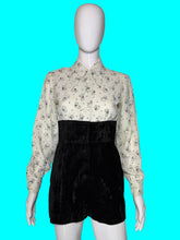 Load image into Gallery viewer, A one piece romper displayed on a white mannequin,  featuring a long-sleeve button-down top with a black cat print on a white background, and high-waisted black velvet shorts.
