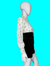 Load image into Gallery viewer, A one piece romper displayed on a white mannequin, featuring a long-sleeve button-down top with a black cat print on a white background, and high-waisted black velvet shorts.
