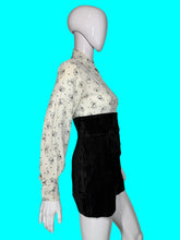 Load image into Gallery viewer, A one piece romper displayed on a white mannequin, featuring a long-sleeve button-down top with a black cat print on a white background, and high-waisted black velvet shorts.

