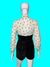 Load image into Gallery viewer, A one piece romper displayed on a white mannequin, featuring a long-sleeve button-down top with a black cat print on a white background, and high-waisted black velvet shorts.
