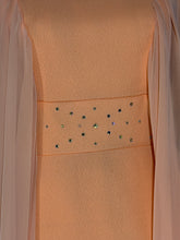 Load image into Gallery viewer, Close-up of a peach-colored dress with a sheer draped overlay and a horizontal band of iridescent rhinestone embellishments across the center.
