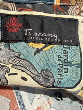 Load image into Gallery viewer, Close-up of a printed garment label reading 'Tuscamy DESIGNS FOR MEN' with a red fleur-de-lis logo on a patterned textile.
