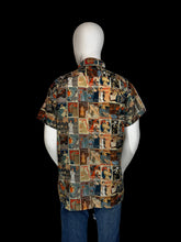 Load image into Gallery viewer, A short-sleeve button-up shirt displayed on a white mannequin. The shirt features a dense collage print of magazine cover illustrations in a multicolor palette of blue, red, beige, and brown.
