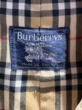 Load image into Gallery viewer, Close-up of a Burberrys label sewn onto a classic plaid patterned fabric, featuring the brand's signature knight embroidered on a blue patch.
