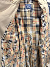 Load image into Gallery viewer, A Burberry coat shown open, featuring the classic beige, navy, and red plaid pattern lining with a solid beige outer fabric.
