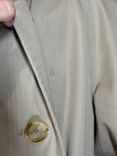 Load image into Gallery viewer, Close-up of a beige trench coat showing a small stain on the fabric and a translucent amber button.
