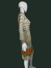 Load image into Gallery viewer, A long-sleeve midi dress with a pleated texture, featuring a beige base with colorful horizontal stripes and a vibrant geometric pattern near the hem, displayed on a white mannequin shown from the side.
