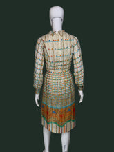 Load image into Gallery viewer, A long-sleeve midi dress with a pleated texture, featuring a beige base with colorful horizontal stripes and a vibrant geometric pattern near the hem, displayed on a white mannequin shown from the back. 
