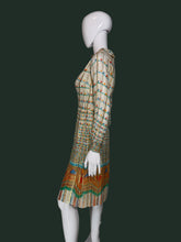 Load image into Gallery viewer, A long-sleeve midi dress with a pleated texture, featuring a beige base with colorful horizontal stripes and a vibrant geometric pattern near the hem, displayed on a white mannequin shown  from the side. 
