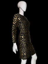 Load image into Gallery viewer, A long-sleeve leopard-print dress displayed on a white mannequin. The dress features a bold black and tan/gold animal print pattern with a button-up front and side pockets.
