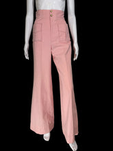 Load image into Gallery viewer, A pair of high-waisted, wide-leg pink pants displayed on a white mannequin. The pants feature a buttoned waistband with gold-tone buttons and two large patch pockets on the front.
