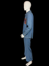 Load image into Gallery viewer, A side view of a blue denim two-piece set consisting of a long-sleeve button-front shirt and matching pants, displayed on a white mannequin. The shirt features colorful embroidered  patterns on the chest in red, orange, and yellow.

