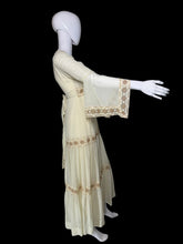 Load image into Gallery viewer, A side view of a cream-colored maxi dress with beige embroidery, shown on a white mannequin with it's arm up to show off the long bell sleeves. 

