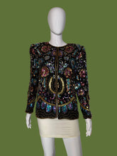 Load image into Gallery viewer, A long-sleeve embellished jacket displayed on a white mannequin. The jacket is heavily decorated with iridescent sequins and beads in black, gold, pink, blue, and green tones, featuring a central gold circular motif.
