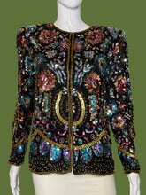 Load image into Gallery viewer, A long-sleeve embellished jacket displayed on a white mannequin. The jacket is heavily decorated with iridescent sequins and beads in black, gold, pink, blue, and green tones, featuring a central gold circular motif.
