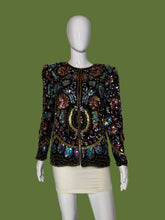 Load image into Gallery viewer, A long-sleeve embellished jacket displayed on a white mannequin. The jacket is heavily decorated with iridescent sequins and beads in black, gold, pink, blue, and green tones, featuring a central gold circular motif.
