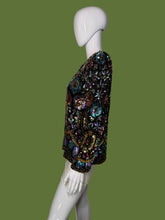 Load image into Gallery viewer, A long-sleeve embellished jacket displayed on a white mannequin. The jacket is heavily decorated with iridescent sequins and beads in black, gold, pink, blue, and green tones, featuring a central gold circular motif.
