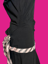 Load image into Gallery viewer, Close-up of a black dress on a mannequin, showing gathered fabric at the waist and a pink, gray, and black striped sash tied at the side.

