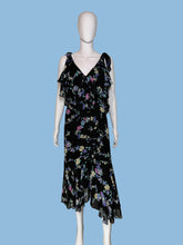 Load image into Gallery viewer, A black sleeveless dress with a colorful floral print, displayed on a white mannequin. The dress features a V-neckline, ruffled shoulder straps, and a tiered ruffle detail at the waist.
