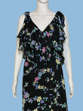 Load image into Gallery viewer, A black sleeveless dress with a colorful floral print, displayed on a white mannequin. The dress features a V-neckline, ruffled shoulder straps, and a tiered ruffle detail at the waist.

