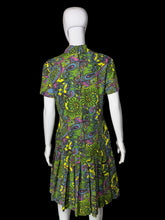 Load image into Gallery viewer, A back view of a short-sleeve collared dress with a vibrant green, yellow, purple, and blue paisley pattern, displayed on a white mannequin against a plain wall.
